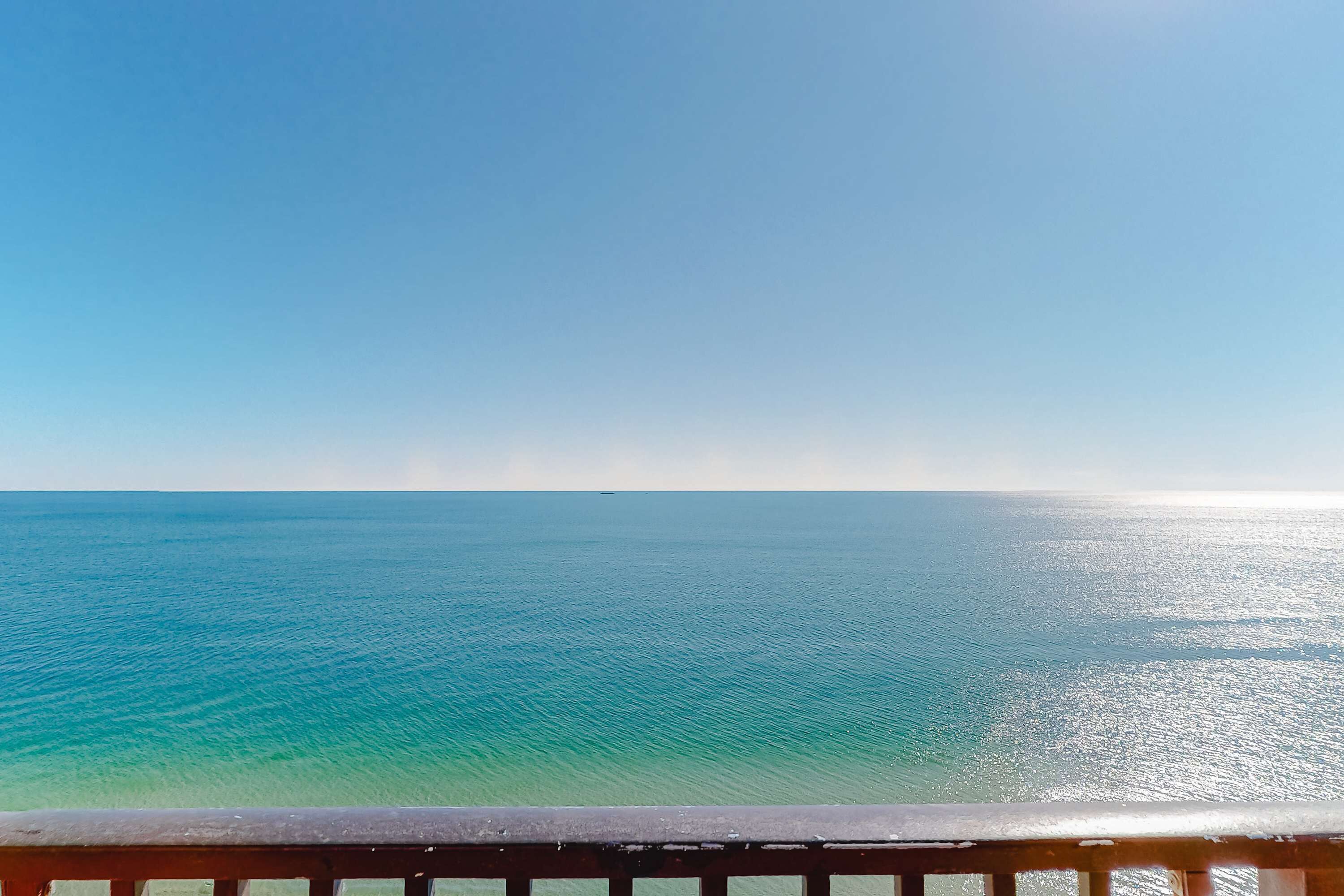 A clear view of the ocean from a balcony with a wooden railing.