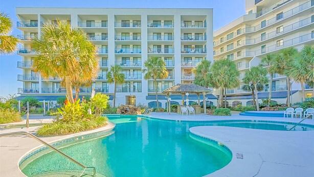 A hotel with a swimming pool, palm trees, and a multi-story building with balconies.