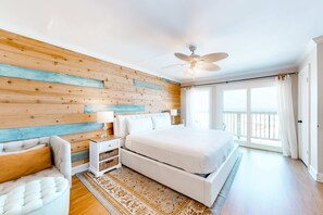 A bedroom with a bed, a nightstand, a chair, a ceiling fan, and a window with curtains. - Gulf-Front Condo w Balcony, Beach Views, WiFi, AC & Shared Gulf-Facing Pool (Gulf Shores)