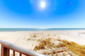 Blick auf den Strand von einem Balkon mit Holzdeck und Geländer.