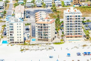Ein Strandhotel mit mehreren Etagen, einem Schwimmbad und einem Strandbereich mit Sonnenschirmen.