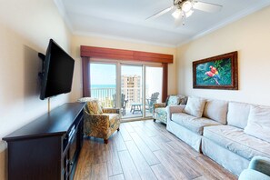 A living room with a flat-screen TV, a sofa, a chair, and a painting on the wall. - Gulf-view condo with pool, hot tub, lazy river & balcony (Gulf Shores)