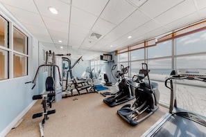 A gym with exercise equipment, large windows, and a view of the beach. - 13th-floor oceanfront condo with balcony, AC, grill, pool, hot tub & gym (Gulf Shores)