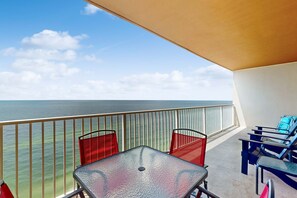 A balcony with a table and chairs, overlooking the ocean. - 13th-floor oceanfront condo with balcony, AC, grill, pool, hot tub & gym (Gulf Shores)