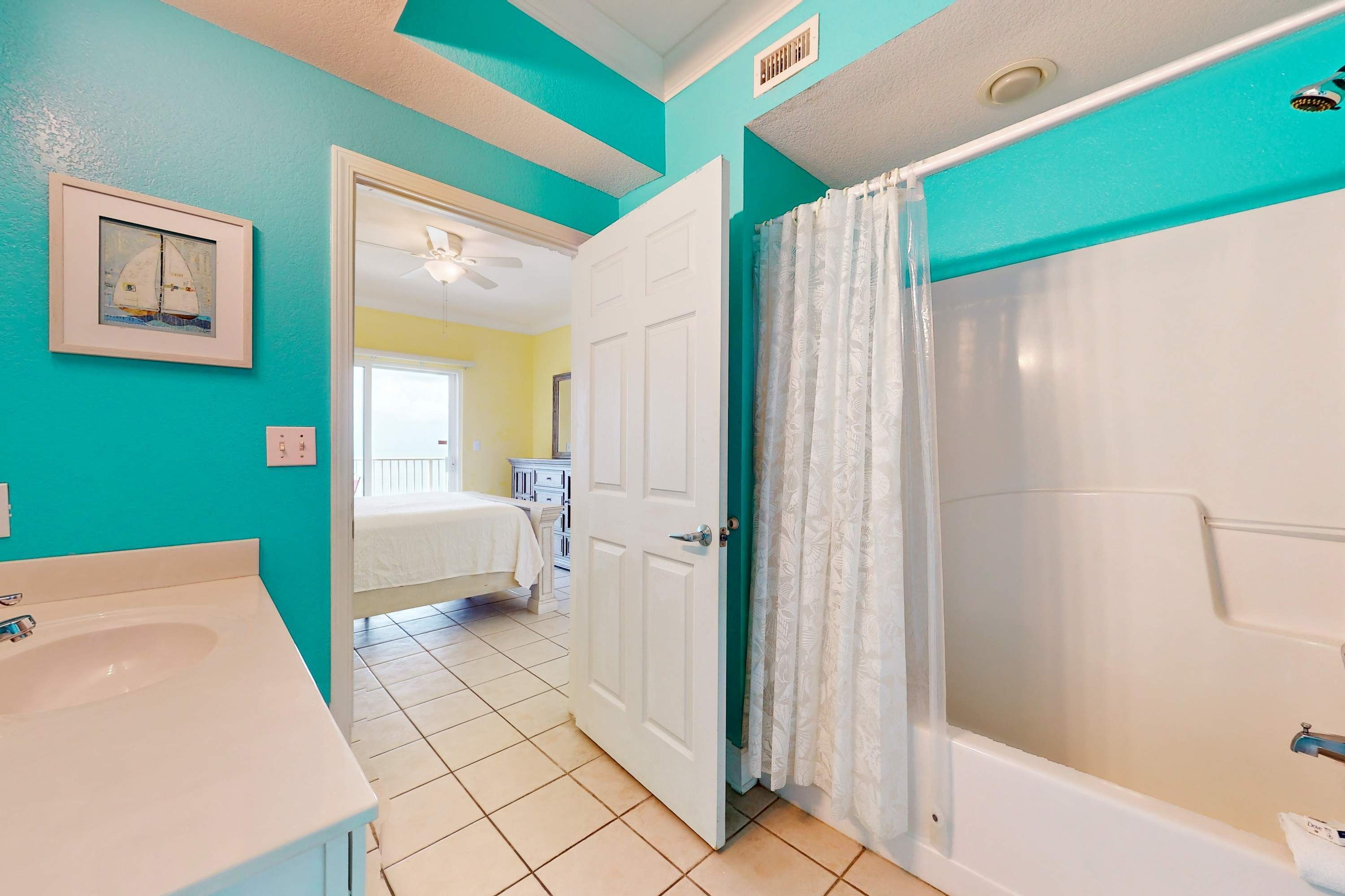 A bathroom with a bathtub, a sink, and a door leading to a bedroom.
