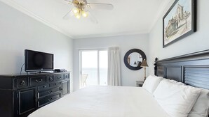Ein Hotelzimmer mit einem Bett, einem Fernseher auf einer Kommode, einem Deckenventilator, einem Fenster mit Vorhängen und einem gerahmten Bild an der Wand.