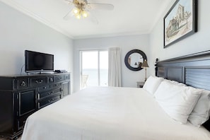 Ein Hotelzimmer mit einem Bett, einem Fernseher auf einer Kommode, einem Deckenventilator, einem Fenster mit Vorhängen und einem gerahmten Bild an der Wand.