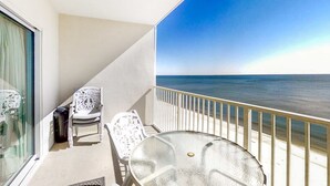 Ein Balkon mit Glastisch und zwei Stühlen, mit Blick auf einen Strand.