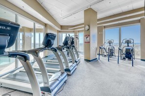 A gym with treadmills, elliptical machines, and a view of the city through large windows. - Gulf-Front Retreat Perfect For Couples w/Shared Pool & Hot Tub, Free WiFi, & W/D (Gulf Shores)