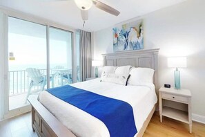 Ett hotellrum med en säng, ett nattduksbord, en takfläkt, en tavla och en balkong med stolar.