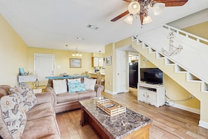 A living room with a brown leather sofa, a marble coffee table, a ceiling fan, a staircase, and a television. - Darling Beach Condo w a Loft, Free WiFi, Balcony, Shared Pool, & Beach Access (Gulf Shores)