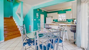 Een keuken met blauwgroene wanden, een eethoek met een glazen tafel en metalen stoelen, en een houten trap.