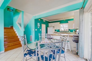 A kitchen with teal walls, a dining area with a glass table and metal chairs, and a wooden staircase. - Bright home with decks, WiFi, AC, laundry & shared pool dock - walk to the beach (Gulf Shores)