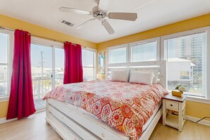 A bedroom with a bed, a nightstand, a ceiling fan, and large windows with curtains. - Bright home with decks, WiFi, AC, laundry & shared pool dock - walk to the beach (Gulf Shores)