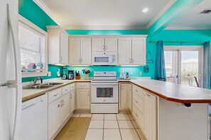 A kitchen with white cabinets, a microwave, a stove, and a sink. - Bright home with decks, WiFi, AC, laundry & shared pool dock - walk to the beach (Gulf Shores)