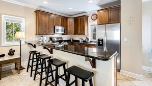 Una cocina con armarios de madera, un refrigerador de acero inoxidable, un microondas y una encimera de granito.