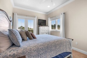 Ein Schlafzimmer mit Bett, Kommode, Fernseher und einem Fenster mit Vorhängen.