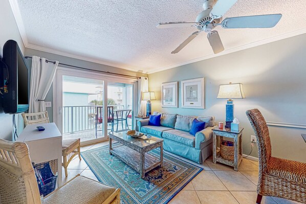 A living room with a sofa, coffee table, and chairs, a ceiling fan, and a view to the outside. - Cheerful beach stay with heated pool, balcony, gulf views, W&D, & central AC (Gulf Shores)