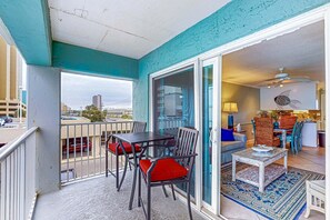 A balcony with a table and chairs, a sliding glass door leading to a living area, and a view of the cityscape. - Cheerful beach stay with heated pool, balcony, gulf views, W&D, & central AC (Gulf Shores)