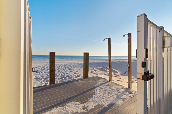 Eine Holzterrasse führt zu einem Strand bei blauem Himmel.