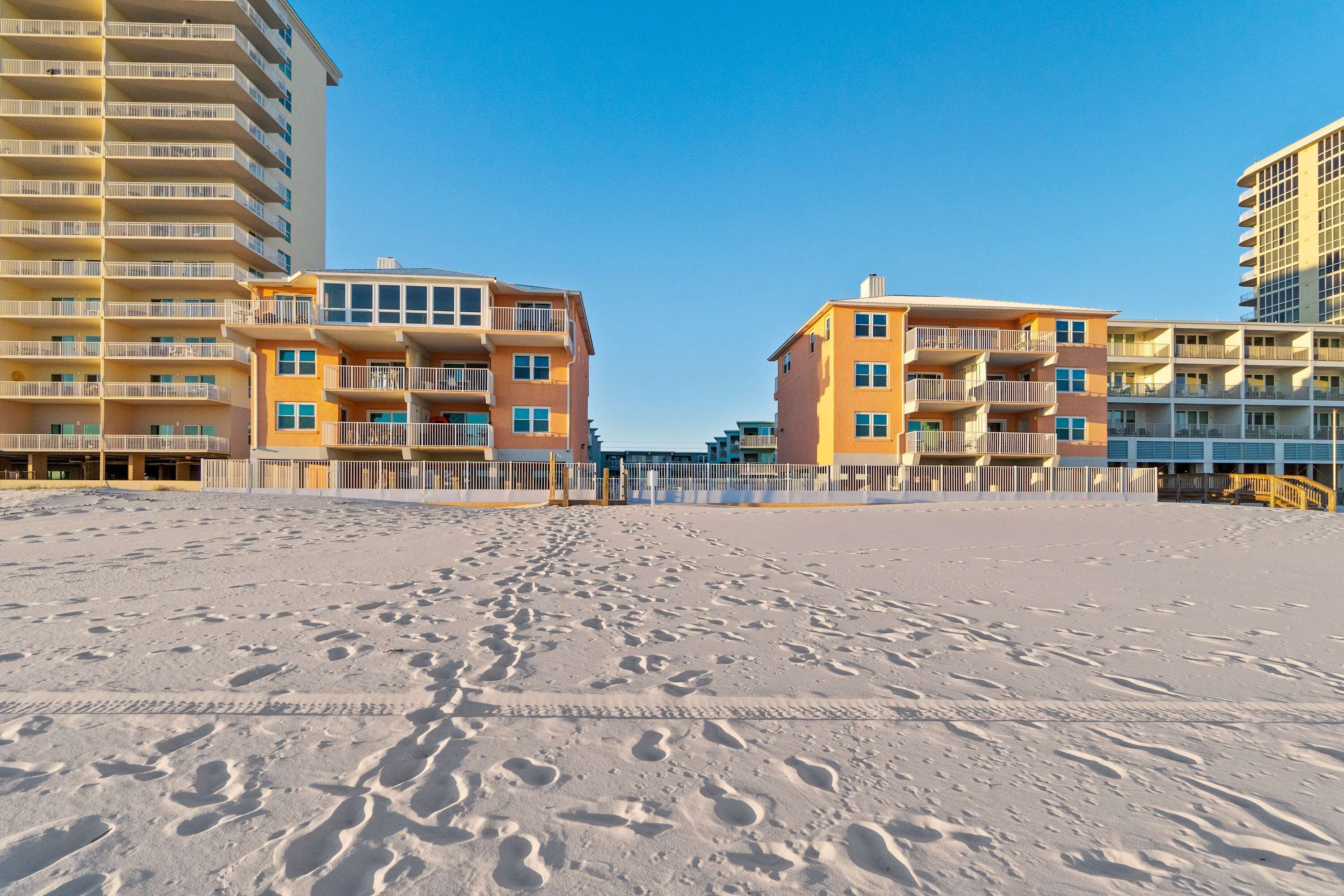 Uma praia com pegadas que levam a uma fileira de edifícios altos com varandas.