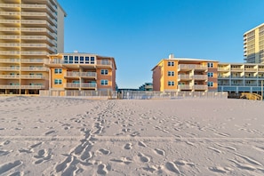 Ein Strand mit Fußspuren, die zu einer Reihe mehrstöckiger Gebäude mit Balkonen führen.