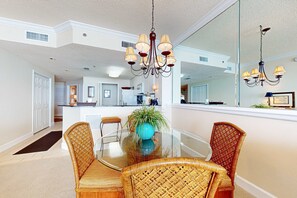 A dining area with a glass table, wicker chairs, a blue vase, and a chandelier. - Gulf-front 10th-floor condo with beach views, sauna, gym, volleyball, pools, AC (Gulf Shores)