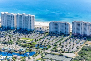 A high-rise hotel complex with multiple buildings, a parking area, and a beach in the background. - Gulf-front 10th-floor condo with beach views, sauna, gym, volleyball, pools, AC (Gulf Shores)