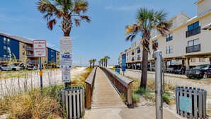 Ein Gehweg führt zu Gebäuden am Strand, Palmen und einem Schild, das nur Rettungsfahrzeugen den Zugang erlaubt.