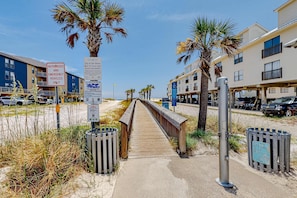 A boardwalk leading to beachside buildings, palm trees, and a sign indicating authorized emergency vehicles only. - New home near the beach with on-site pool,hot tub, private balcony, & W&D (Gulf Shores)