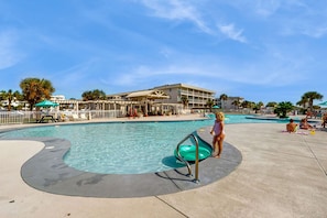 A swimming pool with a lifeguard stand, a covered seating area, and a building in the background. - Beachfront condo with private balcony, pools, tennis, gyms, & saunas (Gulf Shores)