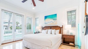 Une chambre avec un grand lit, un ventilateur de plafond, un tableau représentant une plage et une vue à travers les portes coulissantes.