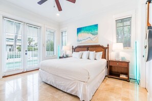 Une chambre avec un grand lit, un ventilateur de plafond, un tableau représentant une plage et une vue à travers les portes coulissantes.