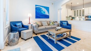 Un salon comprenant un canapé, deux fauteuils, une table basse et un tableau représentant une vague.