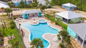 Vue aérienne d’un complexe hôtelier doté d’une grande piscine, de nombreuses chaises longues et d’une terrasse en bois.