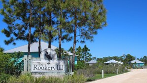 Une enseigne pour « The Rookery III », avec un logo représentant un oiseau, entourée d’arbres et d’un chemin de terre.