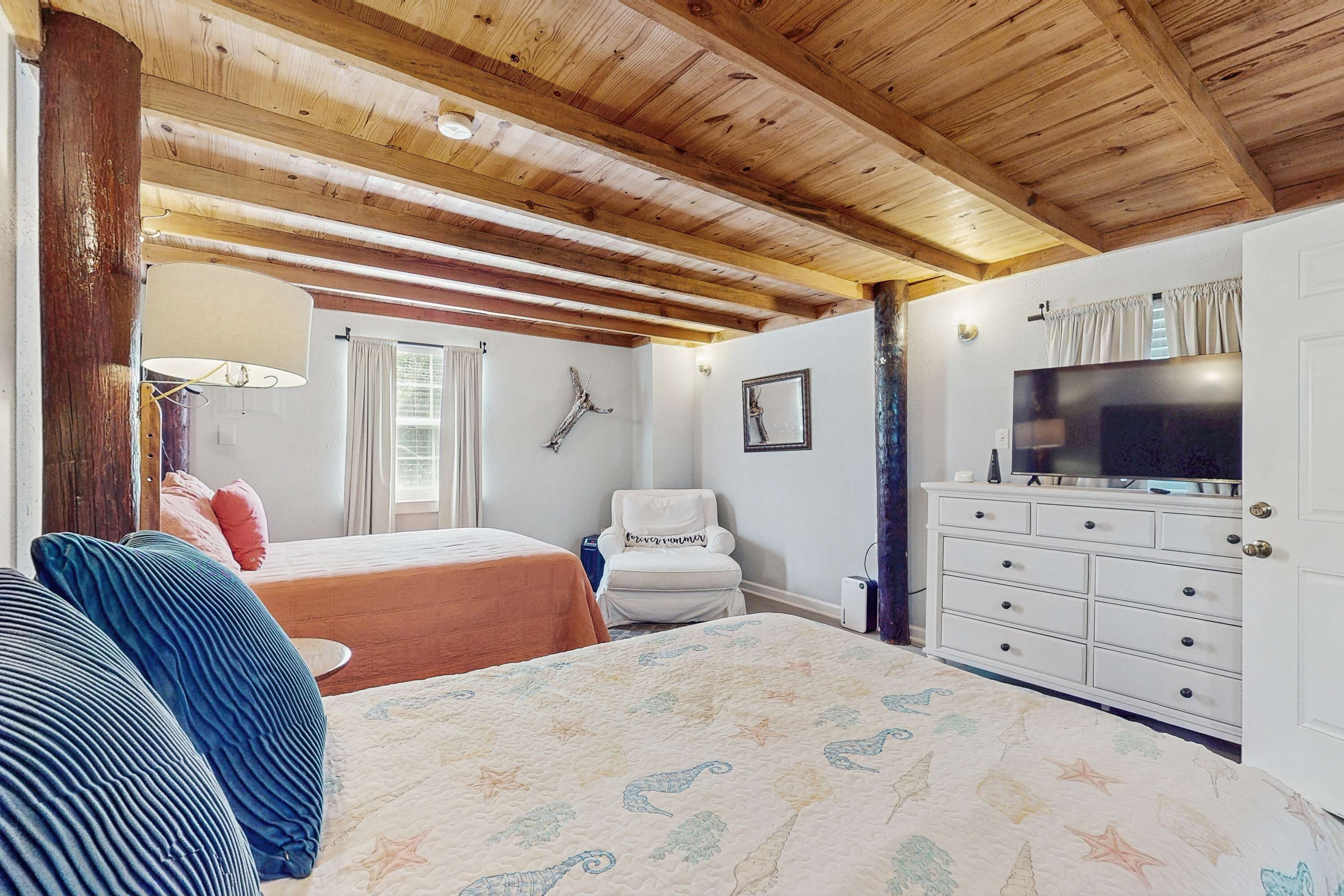 Une chambre avec deux lits, une commode, un téléviseur et un plafond avec des poutres apparentes.