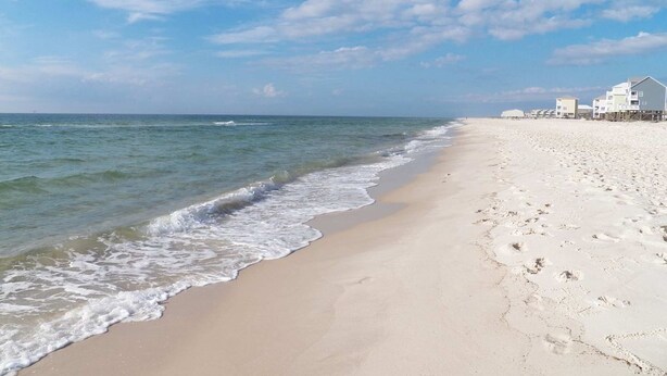 En strand med klart himmel, bølger og bygninger ved strandkanten.
