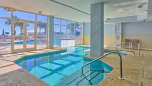 En indendørs swimmingpool med glasvægge, et synligt nødskilt og et bassin med liggestole.