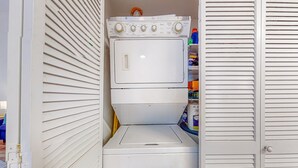 Une buanderie équipée d’un lave-linge et d’un sèche-linge superposés, d’une étagère contenant des produits de nettoyage et d’une porte dotée d’une poignée.