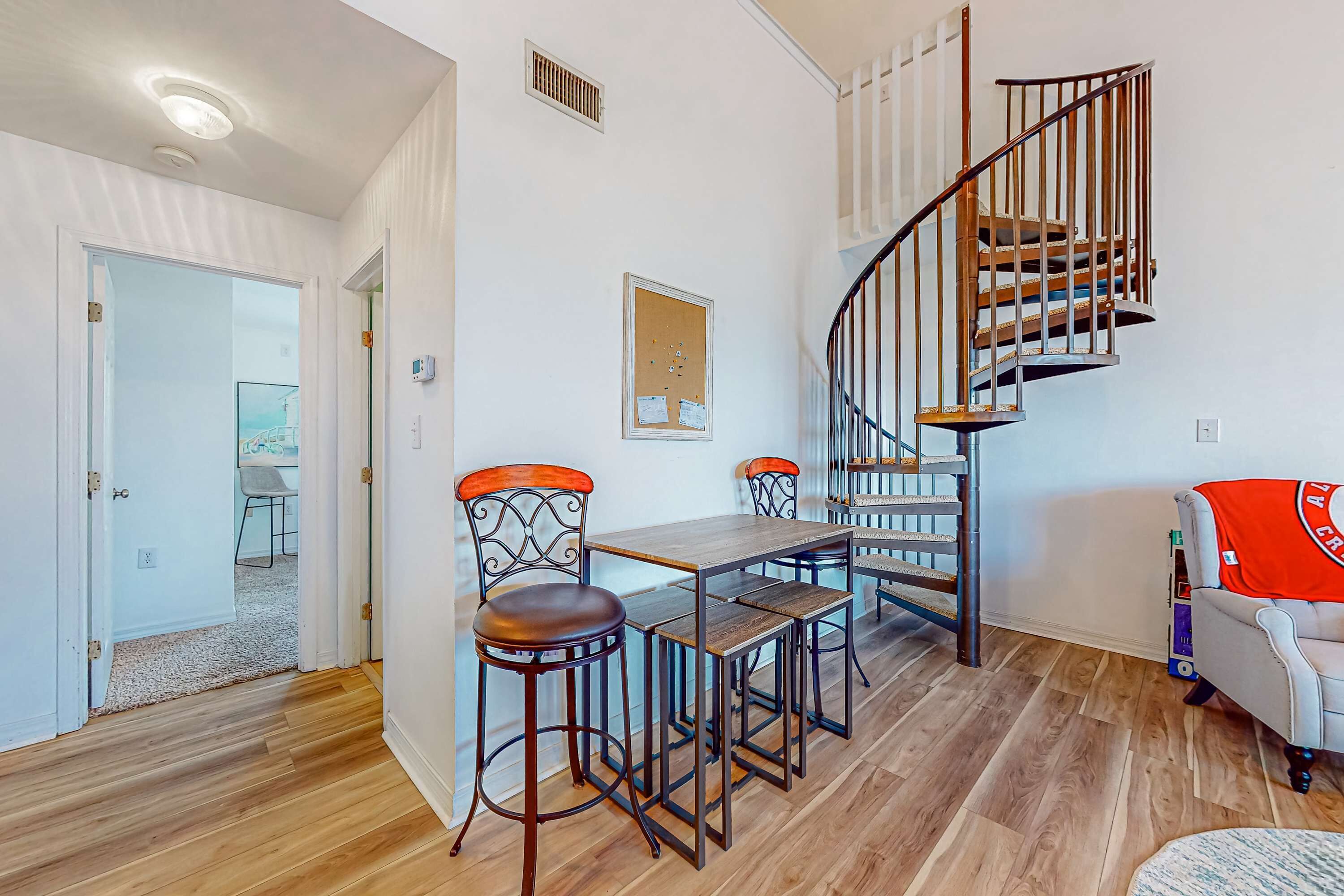 A dining area with a wooden table and chairs, a spiral staircase, and a view of the outside.