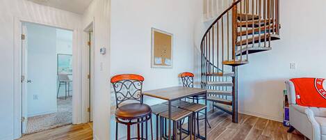 A dining area with a wooden table and chairs, a spiral staircase, and a view of the outside.