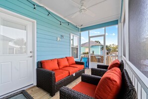 A covered porch with a blue exterior wall, wicker furniture, and a white door. - Brand-new cottage with covered patio, central AC, W&D, & pool access - near beach (Gulf Shores)