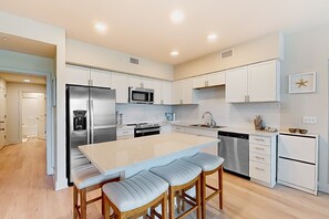 A modern kitchen with a central island, stainless steel appliances, and white cabinetry. - Brand-new beach condo with pool, hot tub, AC & washer/dryer (Gulf Shores)