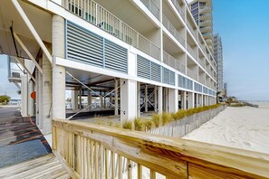 A multi-story hotel with balconies, a covered outdoor area, and a sandy beach in the background. - Brand-new beach condo with pool, hot tub, AC & washer/dryer (Gulf Shores)