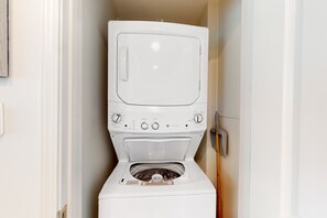 A compact, white front-loading washing machine in a narrow hallway. - Brand-new beach condo with pool, hot tub, AC & washer/dryer (Gulf Shores)