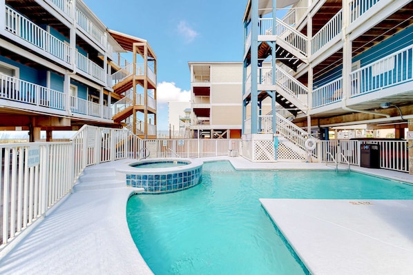 A swimming pool area with a hot tub, surrounded by multi-story buildings with balconies and railings. - Beachfront condo with pool, hot tub, beach access & full kitchen (Gulf Shores)