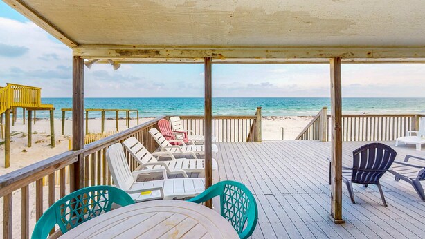 Una terraza de madera con sillas y una mesa, con vistas a la playa.