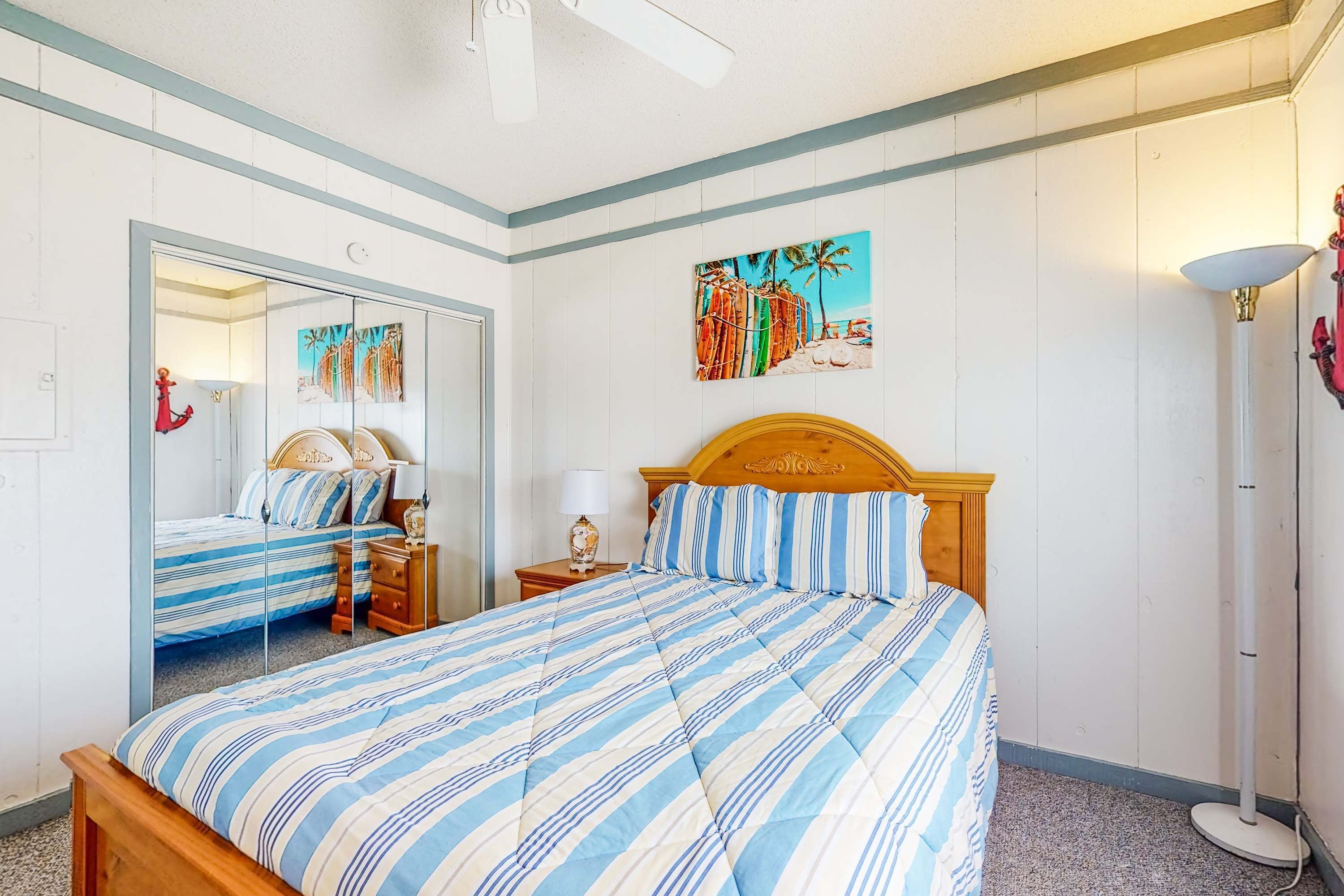 Een slaapkamer met een bed, een spiegel, een nachtkastje, een lamp, een schilderij en een vloerlamp.