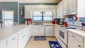 Una cocina con armarios blancos, una ventana con un letrero, un reloj y una estufa.